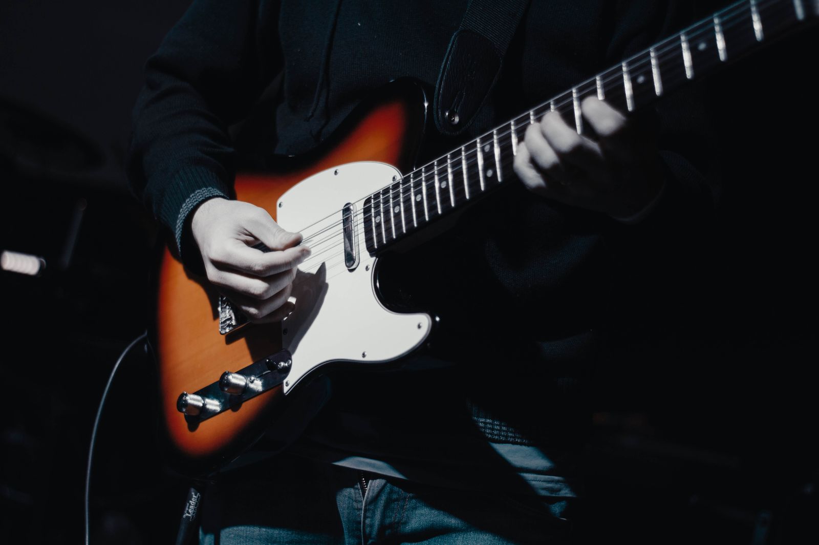 Hands on an electric guitar in dim light